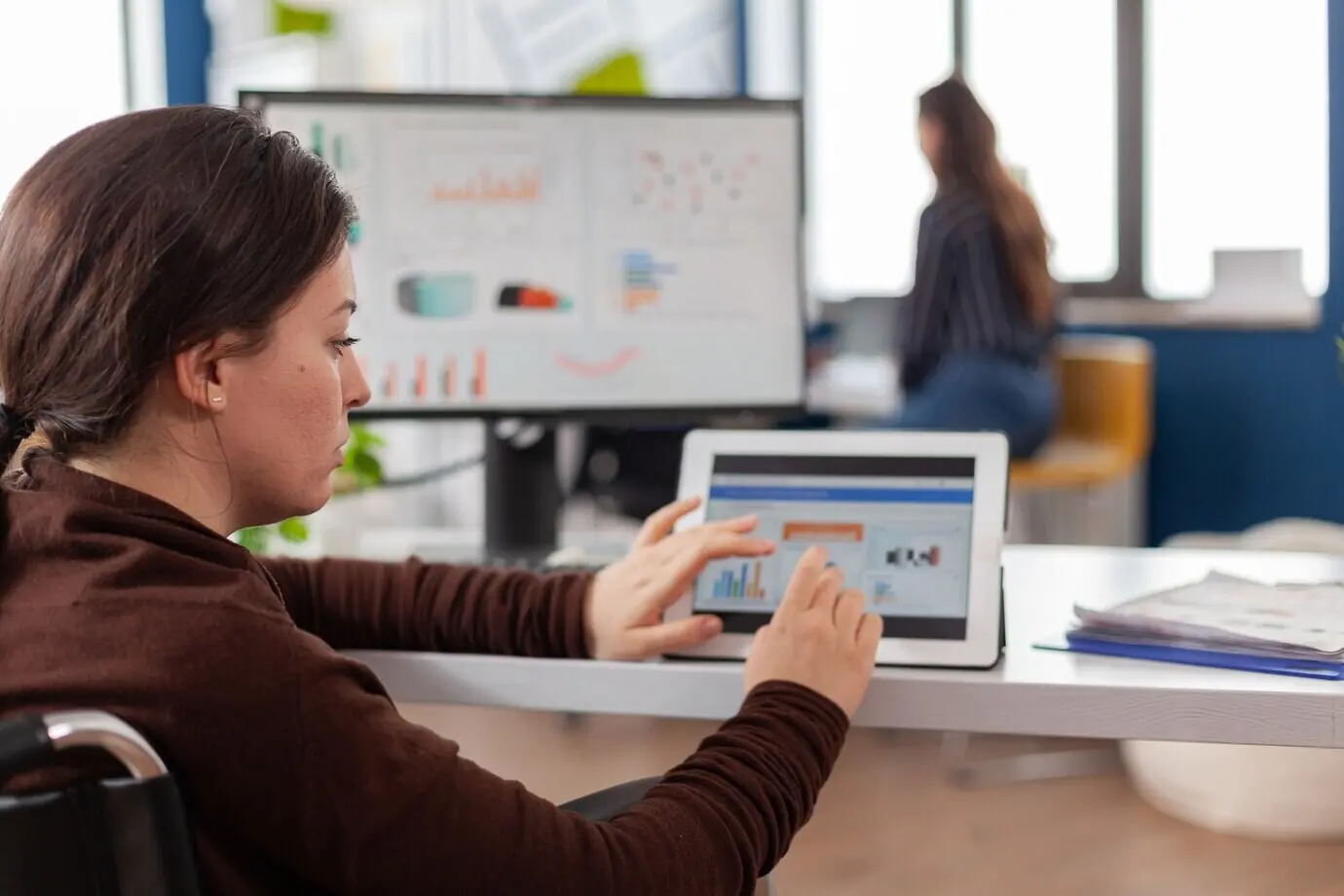 Женщина-предприниматель, используя компьютер и планшет, проверяет статистические данные в офисе стартапа.